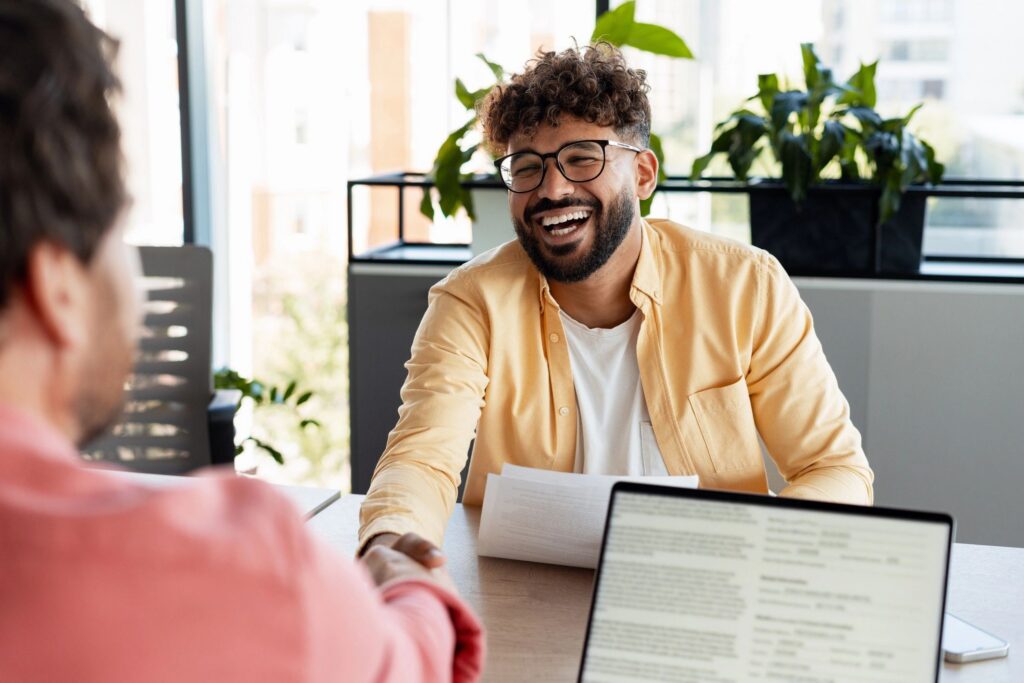 Happy young man shaking hand during job interview in modern office, celebrating success