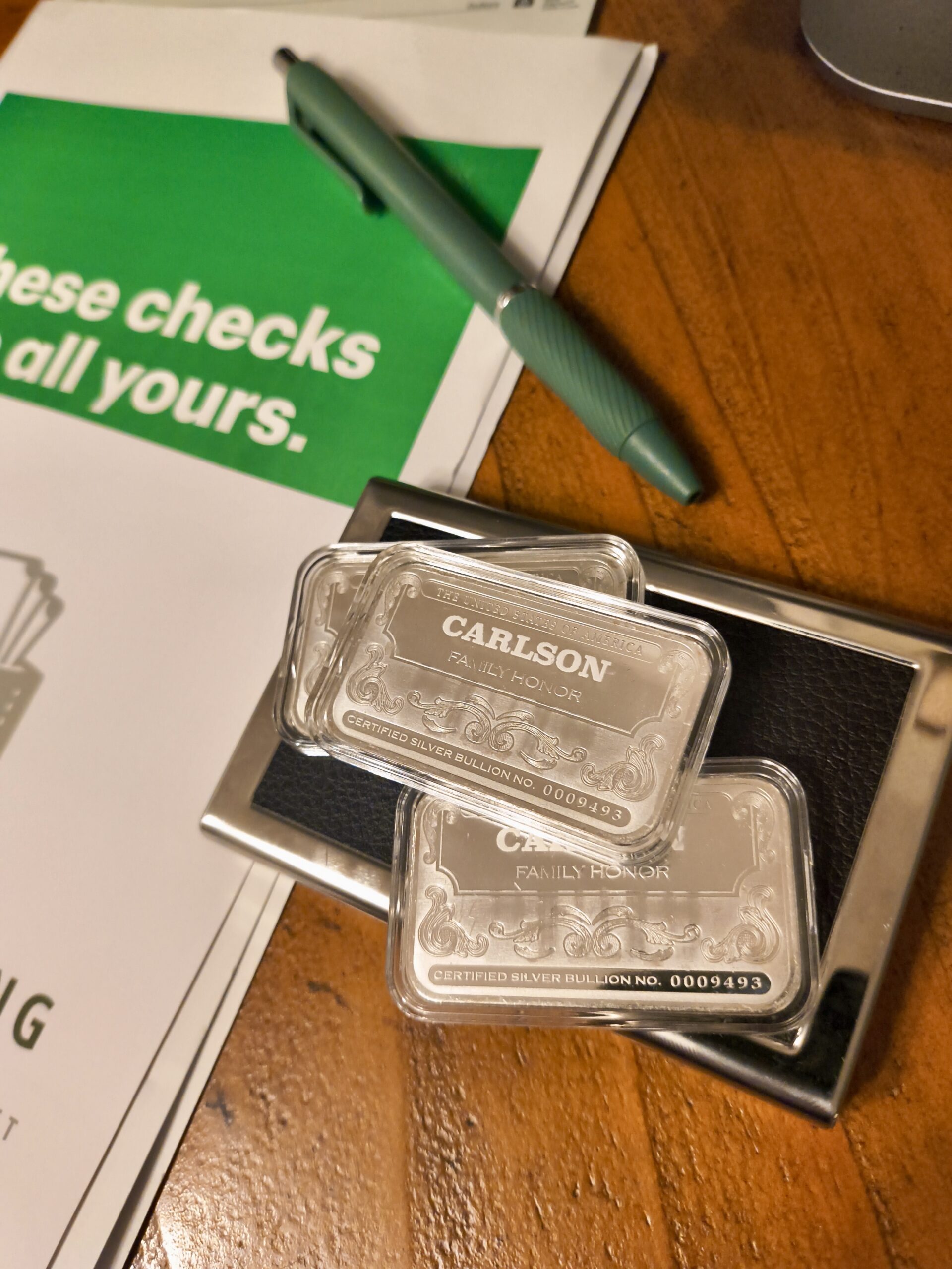 Carlson silver bars on a desk beside paperwork and a green pen
