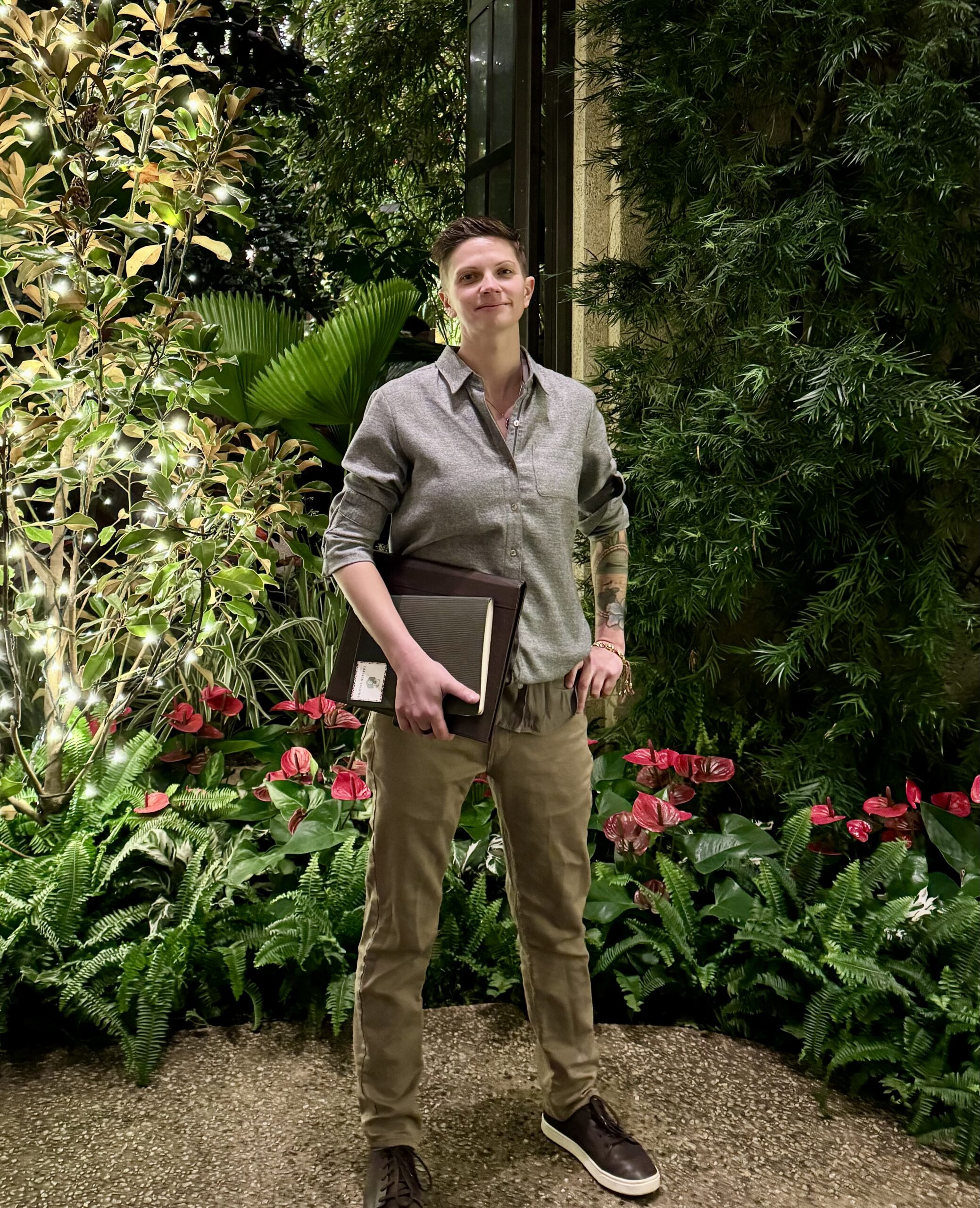 Person standing in a garden courtyard at night holding a folder